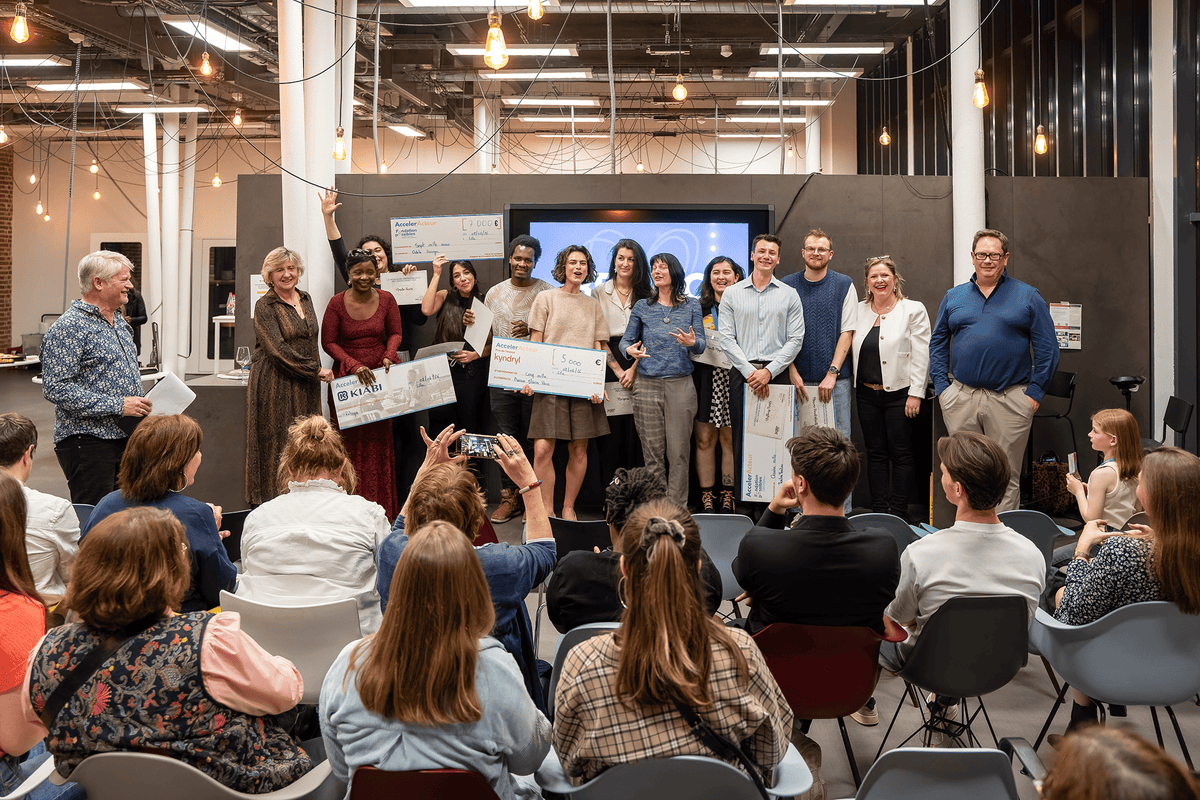 Une remise de prix sur scène devant un public, avec des lauréats souriants brandissant de grands chèques fictifs lors d'un événement de type incubation ou associatif - Fond'Actions des Possibles